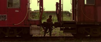 Movie still from “George Washington” (2000), directed by David Gordon Green – A man standing next to a train on a train track; Wide shot, Low angle