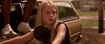 Movie still from “George Washington” (2000), directed by David Gordon Green – A young girl with long blonde hair holding a microphone; Close Up shot, Low angle