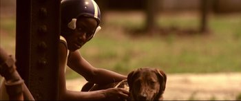 Movie still from “George Washington” (2000), directed by David Gordon Green – A young boy holding a football helmet over a dog's face; Close Up shot, Over the shoulder angle