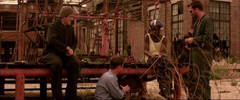 Movie still from “George Washington” (2000), directed by David Gordon Green – A man and a woman sitting on the ground in front of a building; Wide shot, Low angle