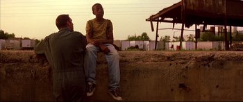 Movie still from “George Washington” (2000), directed by David Gordon Green – A young man sitting on a ledge next to another young man; Medium shot, Over the shoulder angle