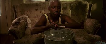 Movie still from “George Washington” (2000), directed by David Gordon Green – A young man is sitting on a couch and holding a bucket; Close Up shot, Low angle