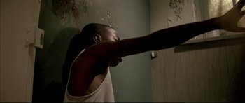 Movie still from “George Washington” (2000), directed by David Gordon Green – A man in a white tank top is in a bathroom; Medium shot, Overhead angle