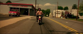 Movie still from “George Washington” (2000), directed by David Gordon Green – A man riding a motorcycle down the middle of the street; Wide shot, Low angle