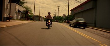 Movie still from “George Washington” (2000), directed by David Gordon Green – A man riding a motorcycle down the middle of the street; Wide shot, Low angle
