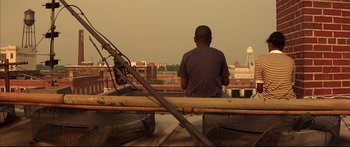 Movie still from “George Washington” (2000), directed by David Gordon Green – A man sitting on top of a bench looking out over a city; Wide shot, Low angle