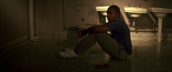 Movie still from “George Washington” (2000), directed by David Gordon Green – A man sitting on the ground holding a nintendo wii game controller; Medium shot, High angle
