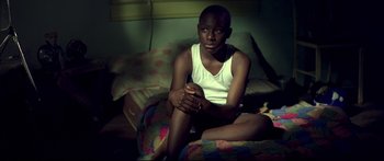 Movie still from “George Washington” (2000), directed by David Gordon Green – A man sitting on top of a bed in the dark; Medium shot, High angle