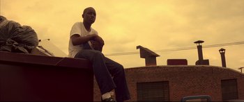 Movie still from “George Washington” (2000), directed by David Gordon Green – A man sitting on top of a brick building; Medium shot, Low angle