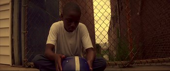 Movie still from “George Washington” (2000), directed by David Gordon Green – A young boy sitting on the ground holding a ball; Medium shot, Low angle