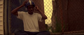 Movie still from “George Washington” (2000), directed by David Gordon Green – A young man wearing a football helmet sitting in front of a chain link fence; Medium shot, Low angle