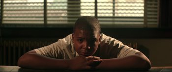 Movie still from “George Washington” (2000), directed by David Gordon Green – A man sitting in front of a window with his hands folded on his chest; Close Up shot, Low angle