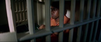 Movie still from “George Washington” (2000), directed by David Gordon Green – A man sitting in front of a cell phone in a jail cell; Medium shot, High angle