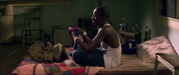 Movie still from “George Washington” (2000), directed by David Gordon Green – A young man sitting on a bed holding a video game controller; Medium shot, Over the shoulder angle