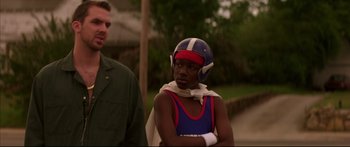 Movie still from “George Washington” (2000), directed by David Gordon Green – A man standing next to another man wearing a helmet; Medium shot, Low angle