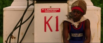 Movie still from “George Washington” (2000), directed by David Gordon Green – A person standing in front of a sign that says k - 1 kerosene; Close Up shot, High angle