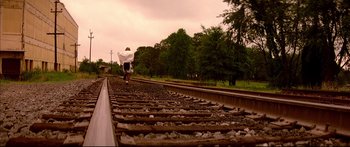 Movie still from “George Washington” (2000), directed by David Gordon Green – A man riding a bike on top of train tracks near trees; Extreme Wide shot, High angle