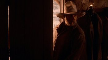 Movie still from “Geronimo: An American Legend” (1993), directed by Walter Hill – A man wearing a cowboy hat standing in front of a window; Medium shot, Low angle