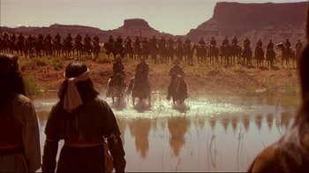 Movie still from “Geronimo: An American Legend” (1993), directed by Walter Hill – A group of men riding horses across a river; Extreme Wide shot, Over the shoulder angle