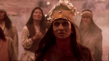 Movie still from “Geronimo: An American Legend” (1993), directed by Walter Hill – A man in a native american costume with other people in the background; Close Up shot, Over the shoulder angle