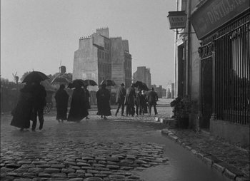 Movie still from “Gervaise” (1956), directed by René Clément – A black and white photo of people walking down the street with umbrellas; Wide shot, High angle