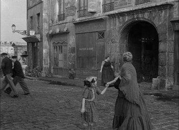 Movie still from “Gervaise” (1956), directed by René Clément – A woman and a child are playing with a frisbee in an old photo; Wide shot, High angle