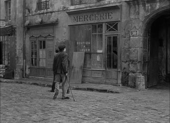 Movie still from “Gervaise” (1956), directed by René Clément – A man walking down the street in front of an old building; Wide shot, High angle