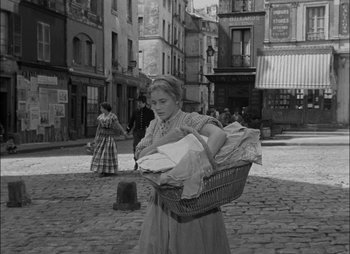 Movie still from “Gervaise” (1956), directed by René Clément – A woman carrying a basket of laundry down a street; Wide shot, High angle