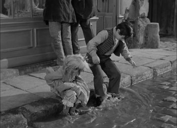 Movie still from “Gervaise” (1956), directed by René Clément – A black - and - white photo of a boy and a girl playing in a puddle; Wide shot, High angle
