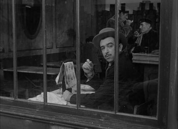 Movie still from “Gervaise” (1956), directed by René Clément – A man sitting at a table in front of a window; Medium shot, Over the shoulder angle