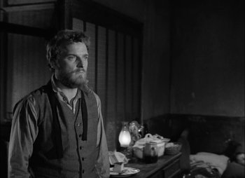 Movie still from “Gervaise” (1956), directed by René Clément – A man standing in front of a table with food on top of it; Medium shot, Over the shoulder angle