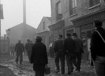 Movie still from “Gervaise” (1956), directed by René Clément – A black and white photo of a group of people walking down a street; Wide shot, High angle