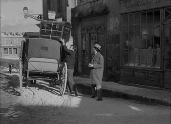 Movie still from “Gervaise” (1956), directed by René Clément – A man standing next to a horse drawn carriage on the side of the street; Wide shot, High angle
