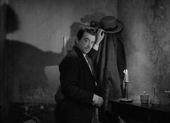 Movie still from “Gervaise” (1956), directed by René Clément – A black and white photo of a man putting on a hat; Medium shot, Low angle