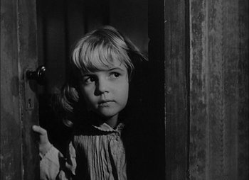 Movie still from “Gervaise” (1956), directed by René Clément – A little girl standing in a doorway looking at the camera; Close Up shot, Over the shoulder angle