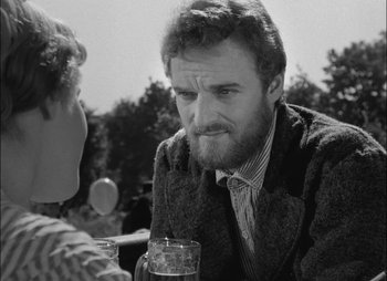 Movie still from “Gervaise” (1956), directed by René Clément – A black and white photo of a man with a beard; Close Up shot, Over the shoulder angle