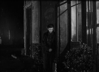 Movie still from “Gervaise” (1956), directed by René Clément – A man standing in front of a building at night; Wide shot, High angle