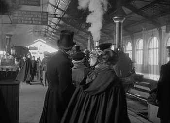 Movie still from “Gervaise” (1956), directed by René Clément – A group of people standing next to each other in front of a train; Wide shot, Over the shoulder angle