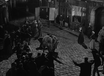 Movie still from “Gervaise” (1956), directed by René Clément – A group of people sitting on top of a brick floor; Extreme Wide shot, High angle