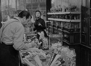 Movie still from “Gervaise” (1956), directed by René Clément – A man and a woman are in a store; Medium shot, High angle