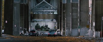 Movie still from “Get Carter” (2000), directed by Stephen Kay – Cars are parked in a parking lot under a bridge; Extreme Wide shot, High angle
