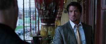 Movie still from “Get Carter” (2000), directed by Stephen Kay – A man wearing a suit and tie standing next to a vase; Close Up shot, Over the shoulder angle