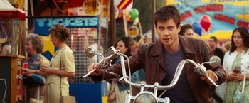 Movie still from “Ghost Rider” (2007), directed by Mark Steven Johnson – A man riding on the back of a motorcycle in front of a crowd; Medium shot, Over the shoulder angle