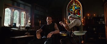 Movie still from “Ghost Rider” (2007), directed by Mark Steven Johnson – A man sitting next to another man in front of a stained glass window; Medium shot, Low angle
