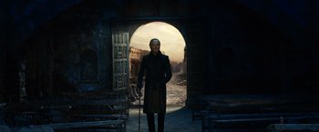 Movie still from “Ghost Rider” (2007), directed by Mark Steven Johnson – A man with a mask and a cane standing in front of an archway; Wide shot, Low angle