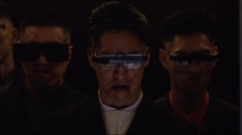 Movie still from “Ghost in the Shell” (2017), directed by Rupert Sanders – A man in a suit and some other men wearing glasses; Close Up shot, Over the shoulder angle