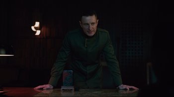 Movie still from “Ghost in the Shell” (2017), directed by Rupert Sanders – A man standing in front of a table with a cell phone on top of it; Medium shot, Over the shoulder angle