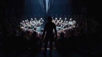 Movie still from “Ghost in the Shell” (2017), directed by Rupert Sanders – A person standing in front of a group of people in a room; Extreme Wide shot, Over the shoulder angle