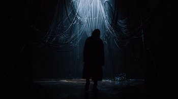 Movie still from “Ghost in the Shell” (2017), directed by Rupert Sanders – A person standing in front of a curtain in a dark room; Extreme Wide shot, Low angle