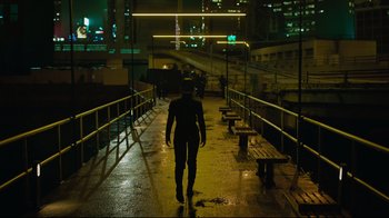 Movie still from “Ghost in the Shell” (2017), directed by Rupert Sanders – A man walking across a bridge at night time; Wide shot, High angle